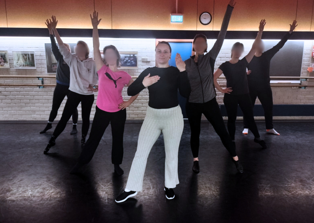 Justyna doet een dansmove met haar dansgroep op de achtergrond in een sportzaal